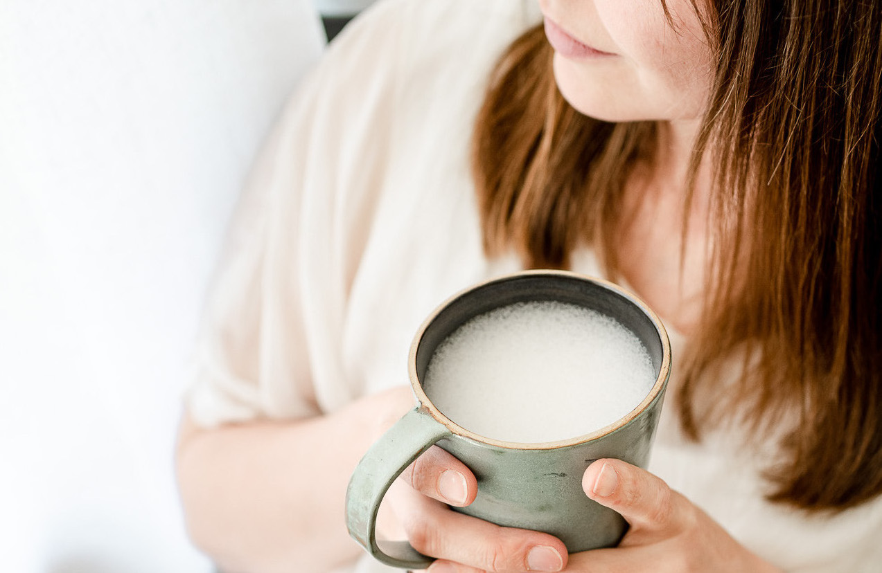 Bildausschnitt entspannt lächelnde Frau mit Kaffee in einem grünen Becher